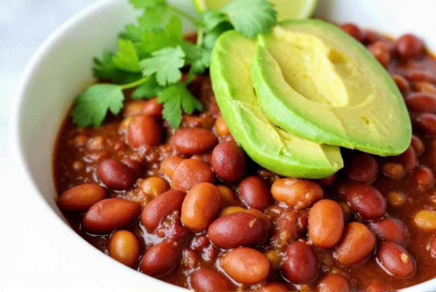 Finished vegan bean chili served in a bowl with avocado slices, cilantro garnish, and lime wedges