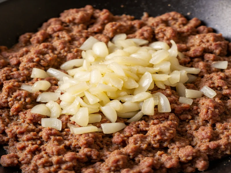 Close-up of diced onions caramelizing in skillet with ground beef