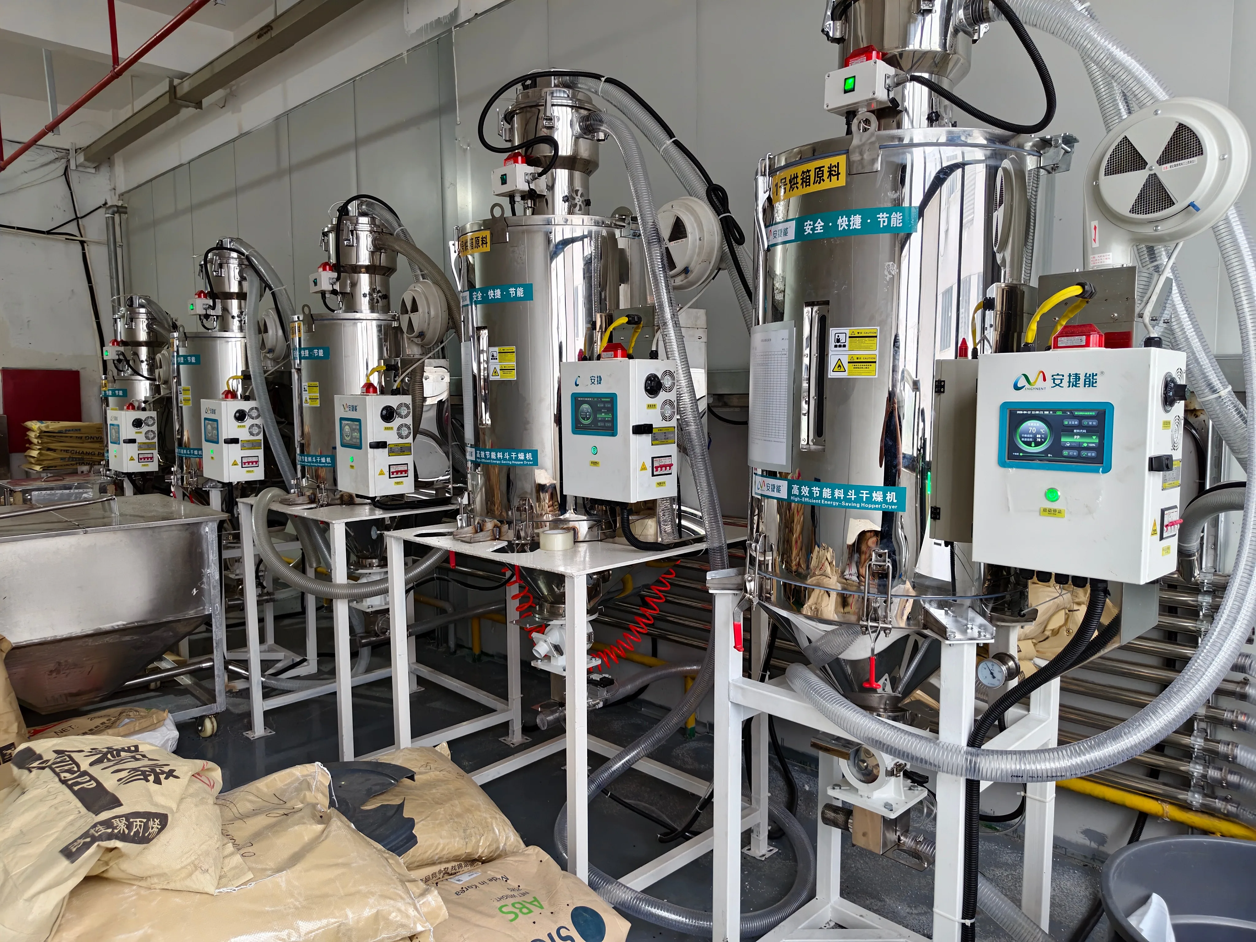 Panorama of the ENGYNENT centralized drying line: a row of high-efficiency energy-saving hopper dryers with overhead centralized feeding pipelines Panorama of the ENGYNENT centralized drying line: a row of high-efficiency energy-saving hopper dryers with overhead centralized feeding pipelines