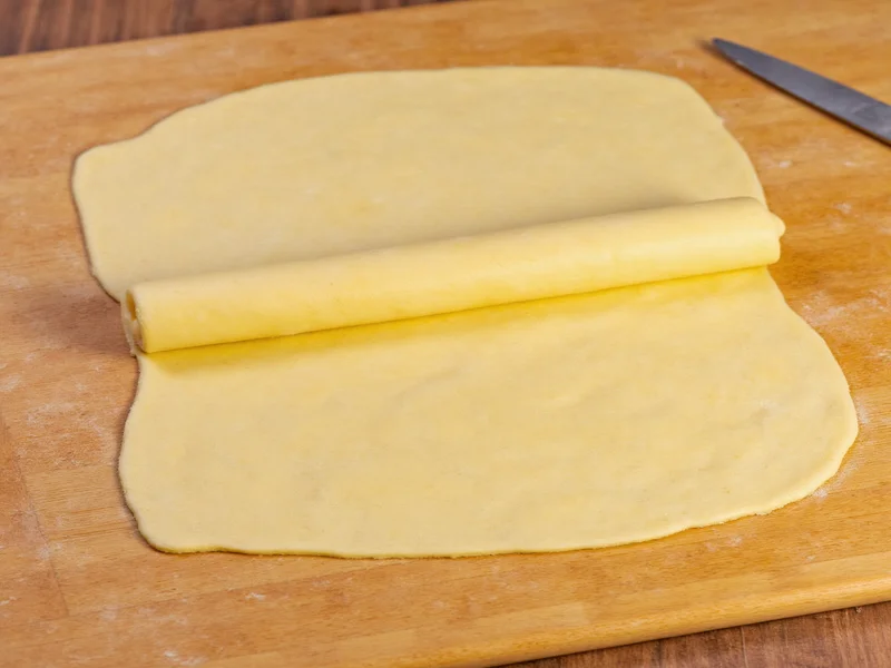 Fresh egg pasta dough rolled into smooth sheet on wooden table