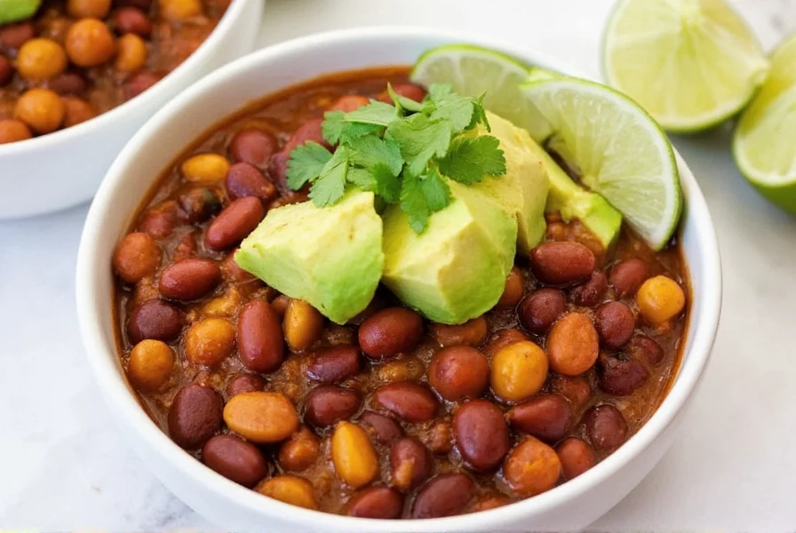 Finished three bean chili served in bowl with avocado, cilantro, and lime wedges as toppings