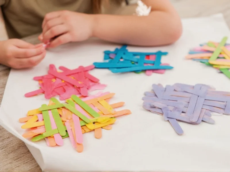 Child's hands gluing colorful popsicle sticks into geometric shapes