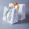 /product-detail/wholesale-cheap-price-custom-logo-white-mini-small-luxury-paperbag-fancy-favor-wedding-door-paper-gift-bag-with-ribbon-handles-62280938415.html