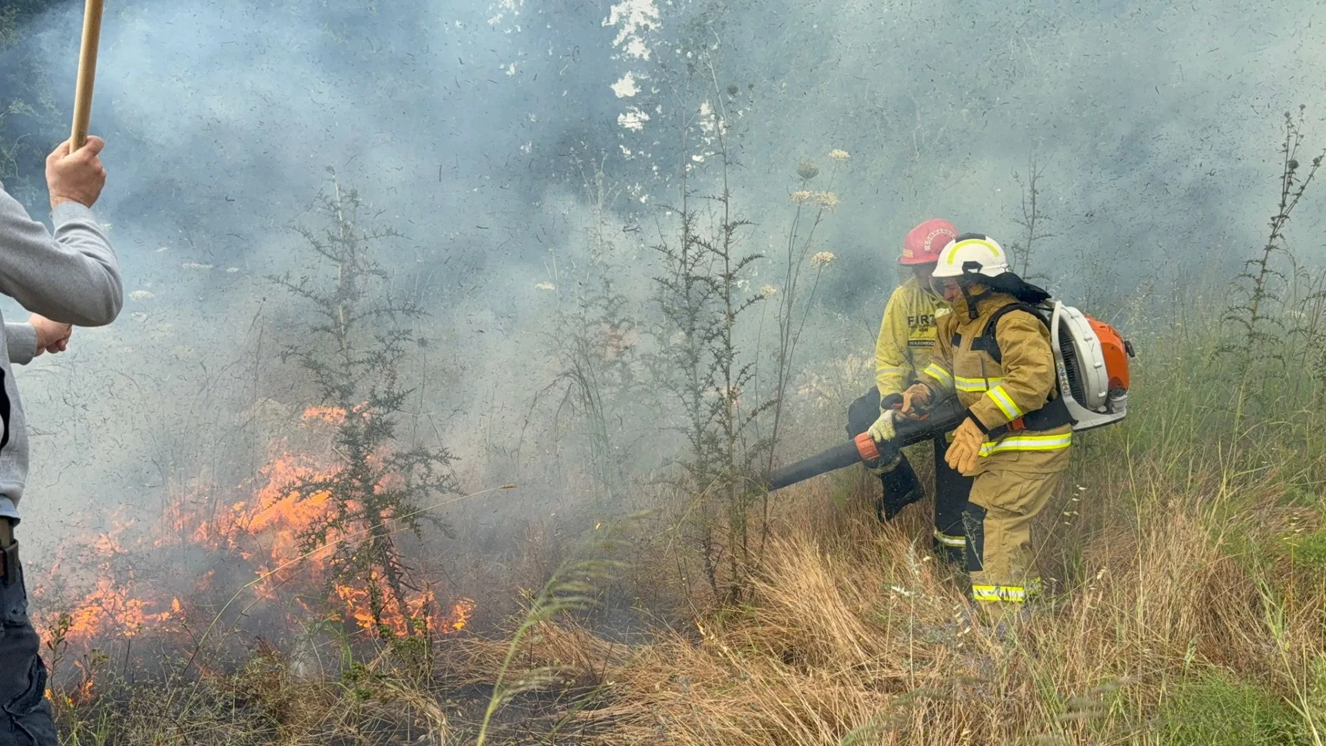 ANBEN FIRE-equipped crew cutting a fire break with a backpack blower as a scrub fire runs upslope
