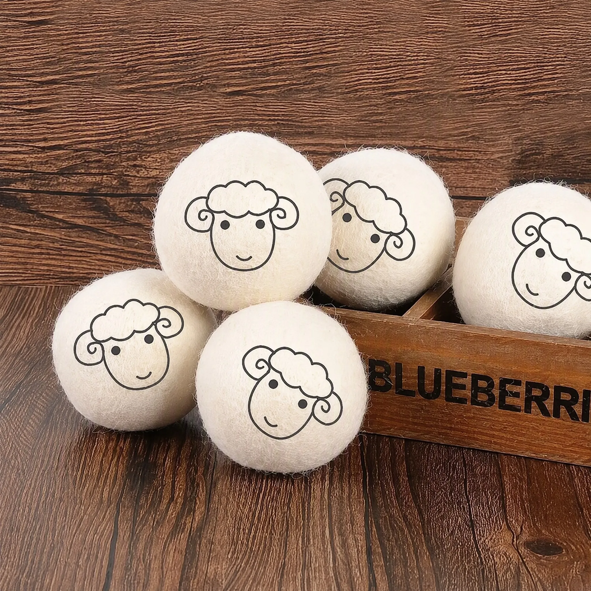 Five logo printed wool dryer balls styled on dark wood with a wooden retail crate