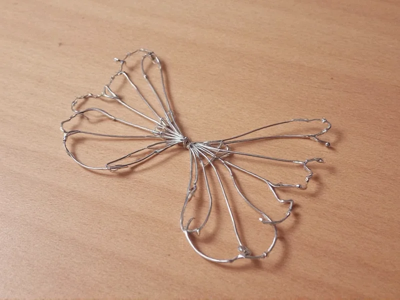 Hand shaping wire frame for fairy wings on wooden surface