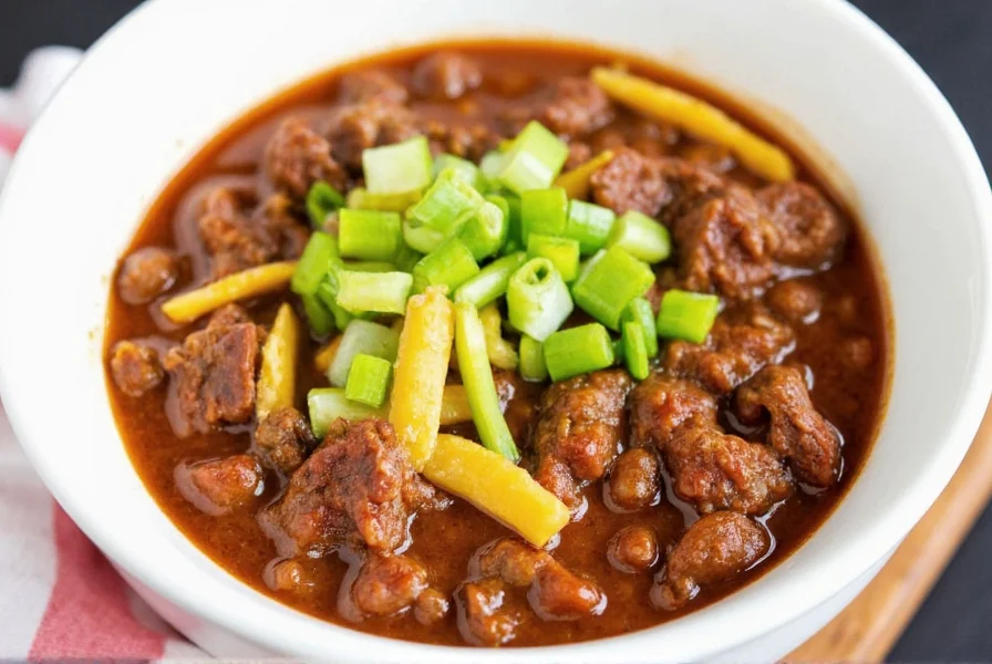 Finished steak chili served in bowl with toppings including cheese, green onions, and avocado