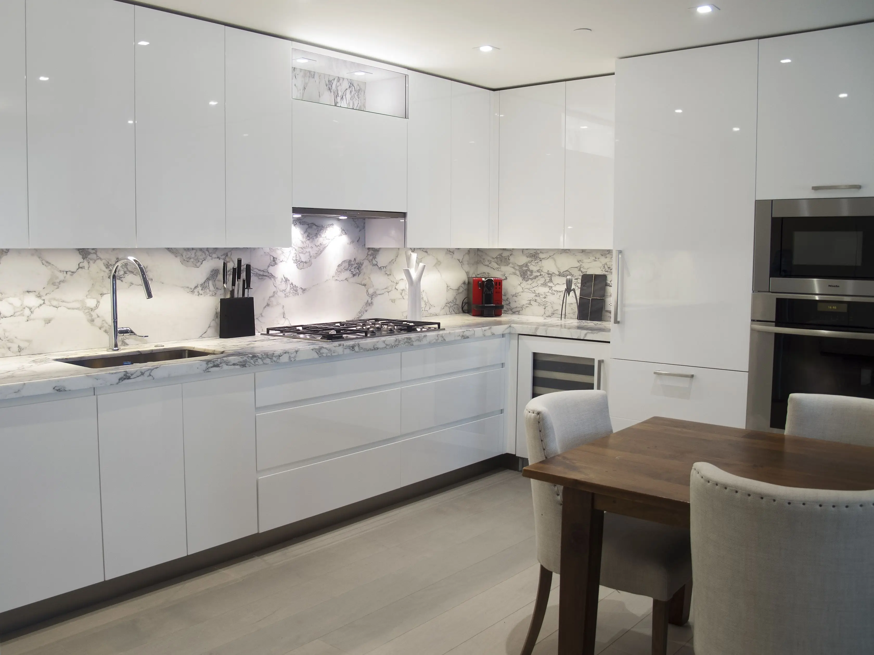 Белая глянцевая кухня с серой столешницей и фартуком в интерьере фото