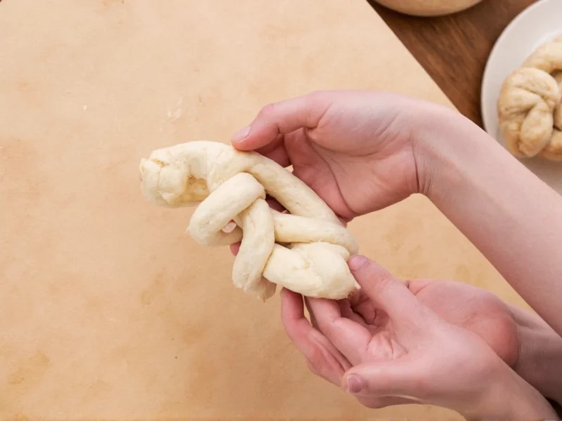 Hands shaping pretzel dough into classic knot