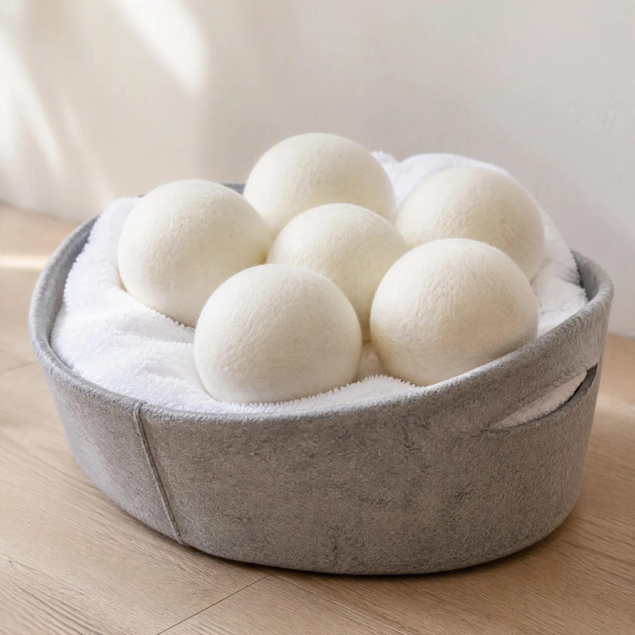 Set of six natural white wool dryer balls stored in a grey felt laundry basket