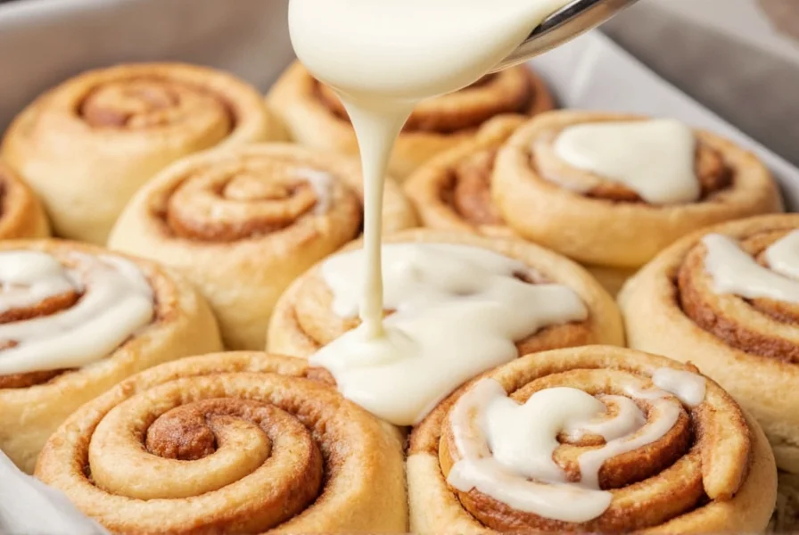 Professional cream cheese frosting being drizzled over freshly baked cinnamon rolls with visible swirls