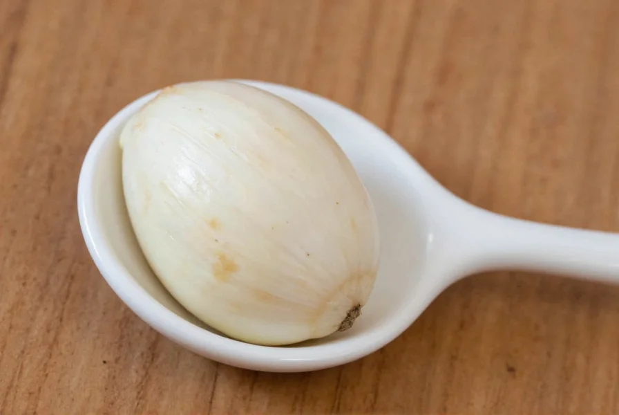 Chef measuring minced garlic in teaspoon next to fresh garlic cloves