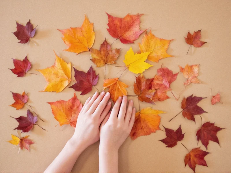 Hand arranging autumn leaves on recycled paper craft