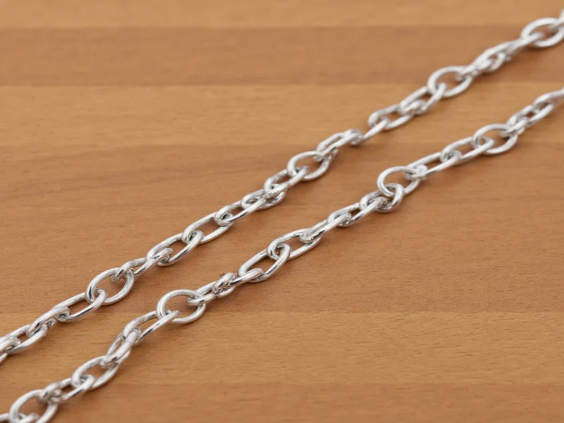 Handmade silver craft chain with alternating jump rings on wooden surface