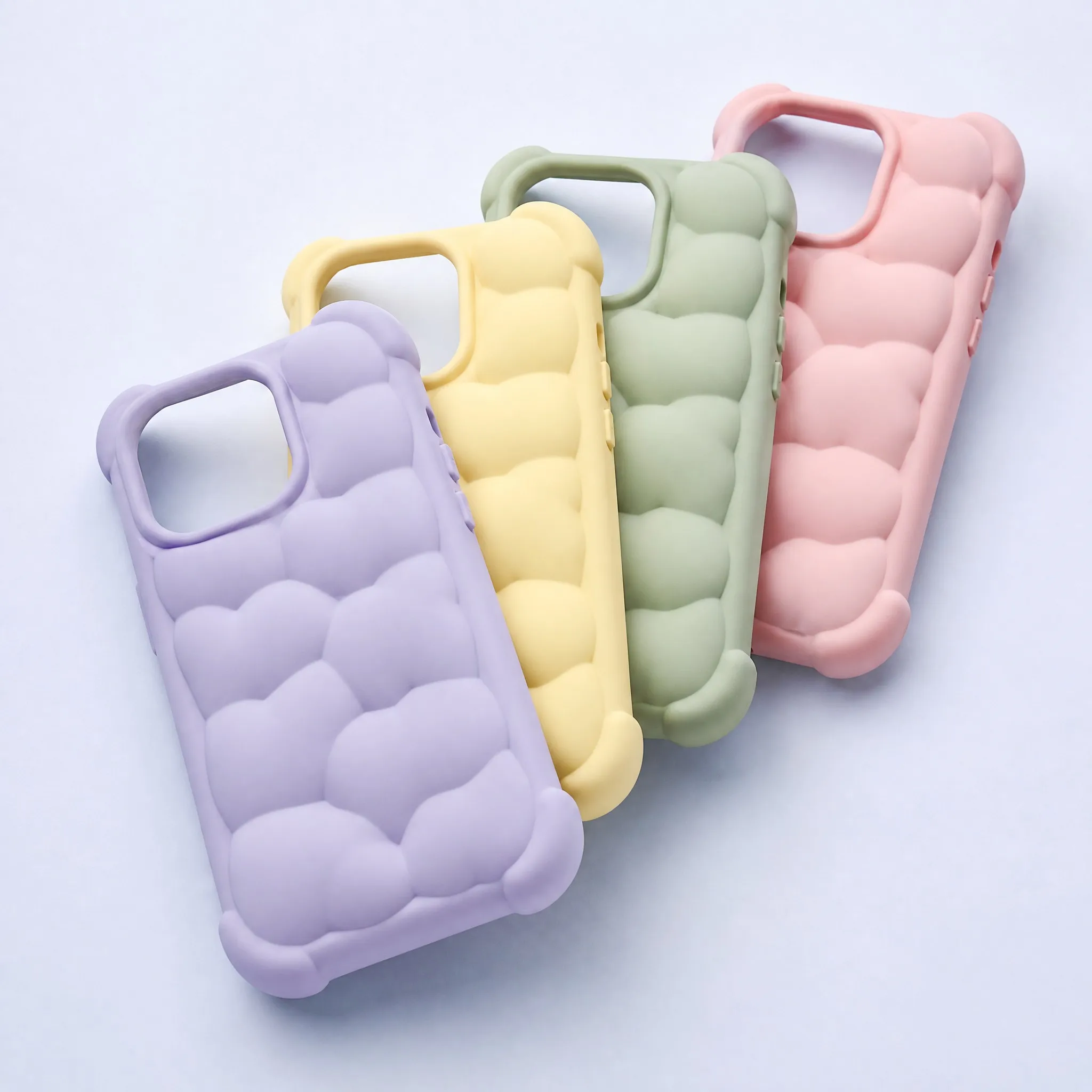 Diagonal Stacking View of 4 Pastel Cloud Puffer Silicone Phone Cases: Purple, Yellow, Green, Pink showing Bubble Ridges