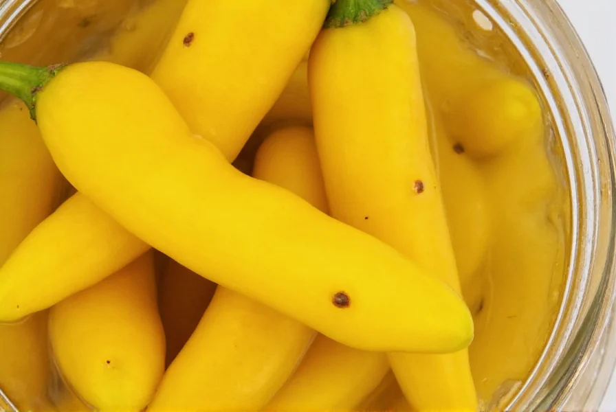 Close-up of crisp yellow pickled banana peppers in glass jar with visible seeds and vinegar brine