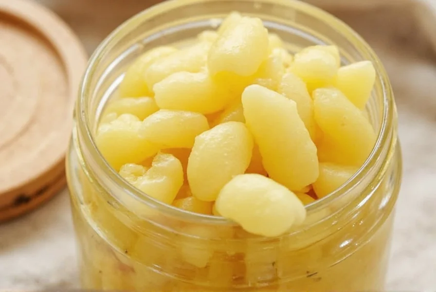 Close-up of thinly sliced young ginger in a glass jar with rice vinegar mixture showing the natural pink hue developing during pickling process