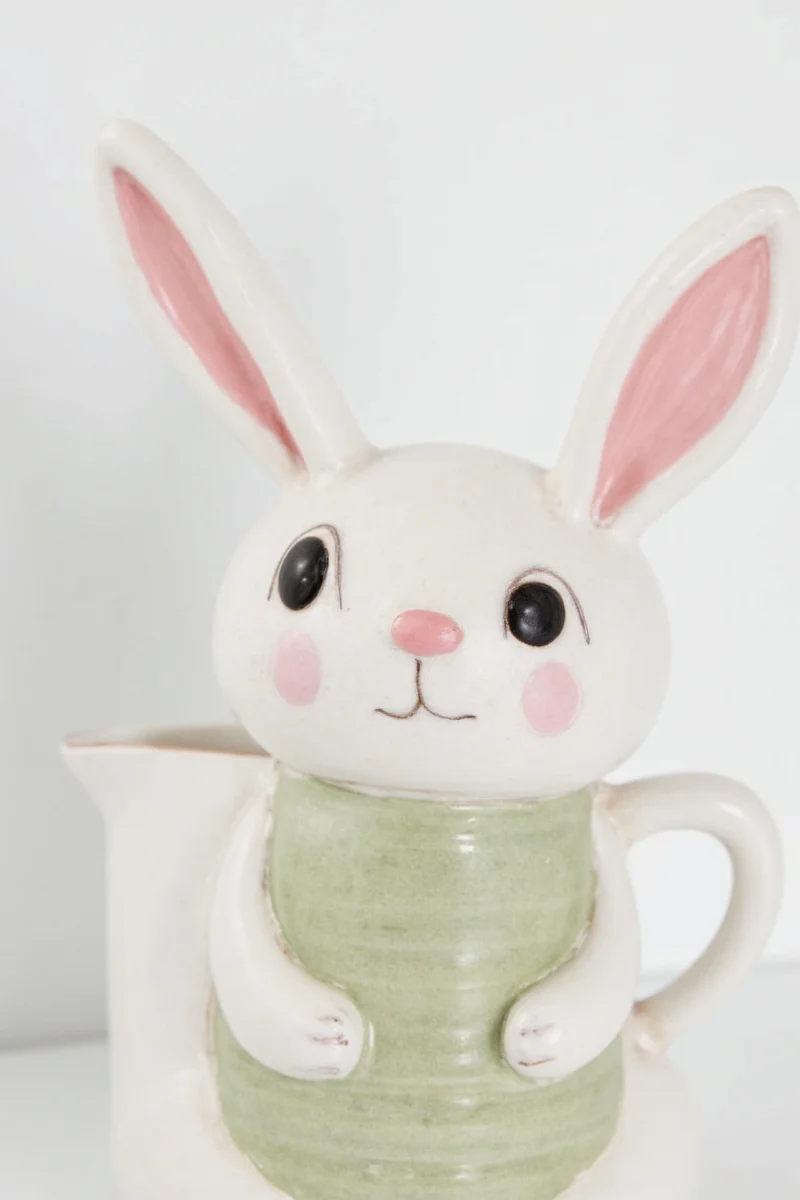 A living room bookshelf featuring a bunny rabbit pitcher nestled between books and decorative candles.