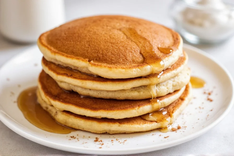 Perfectly golden brown cinnamon pancakes stacked on a plate with maple syrup drizzle and cinnamon stick garnish