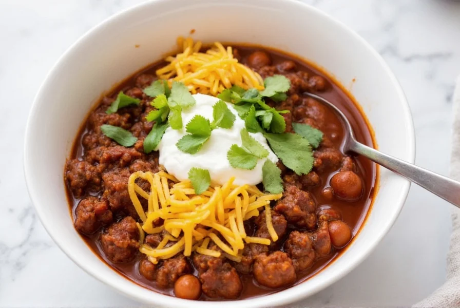 Serving venison chili in bowl with toppings including shredded cheese, sour cream, and fresh cilantro