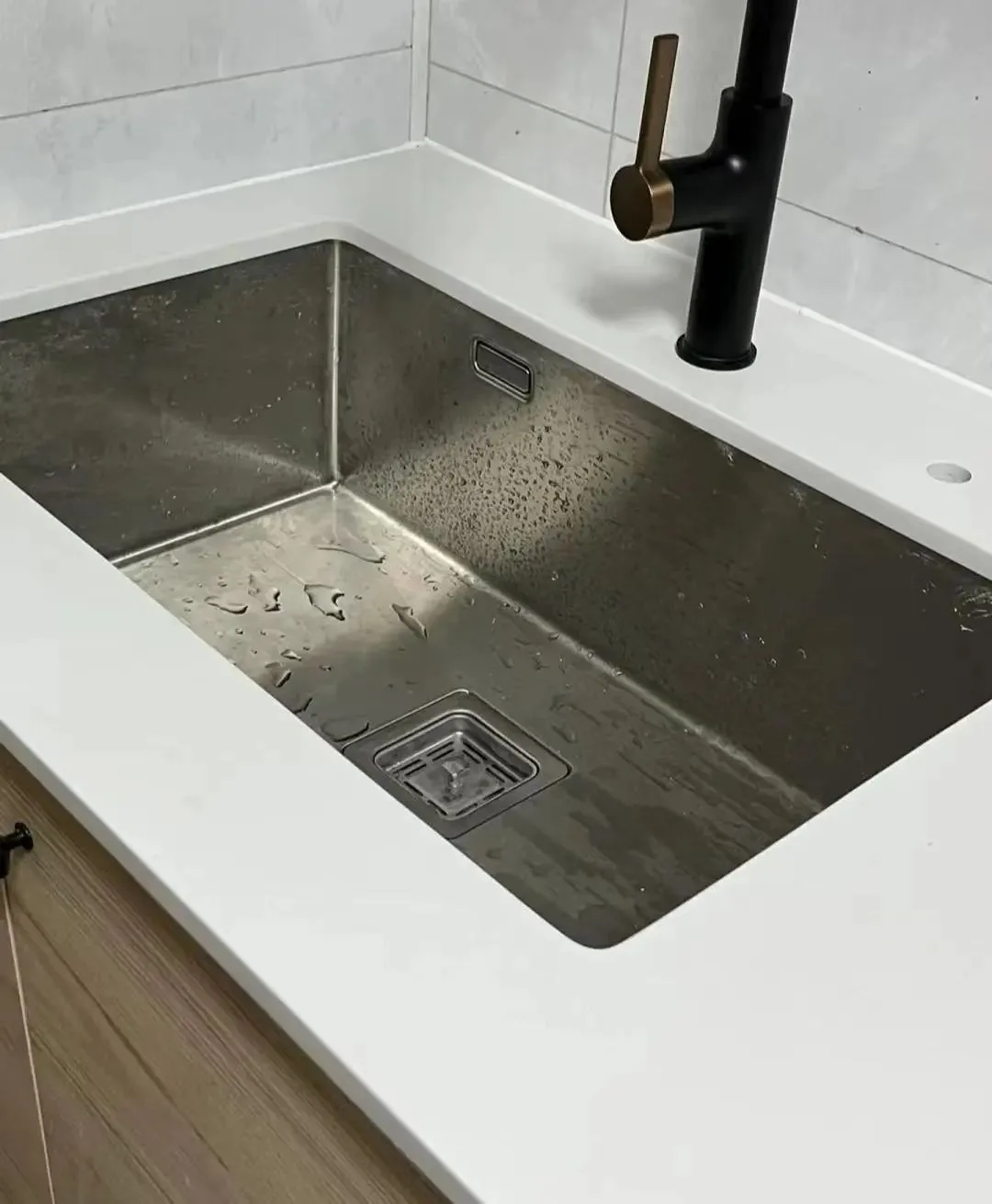 Undermount stainless steel sink cut into a white quartz countertop with a black brass faucet