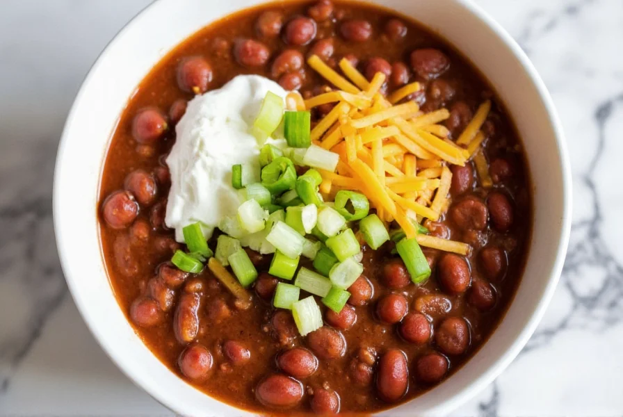 Finished bowl of slow cooker chili with toppings: sour cream, shredded cheese, green onions