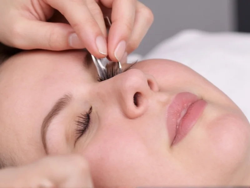 Hand holding curved tweezers applying single lash extension with safety gap