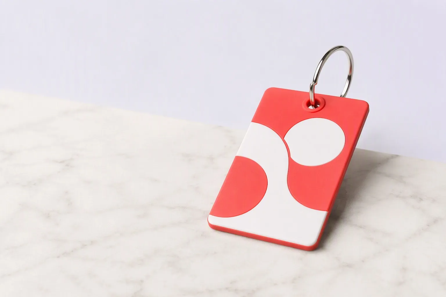 Coral-red and white abstract-pattern PVC keychain leaning on marble surface