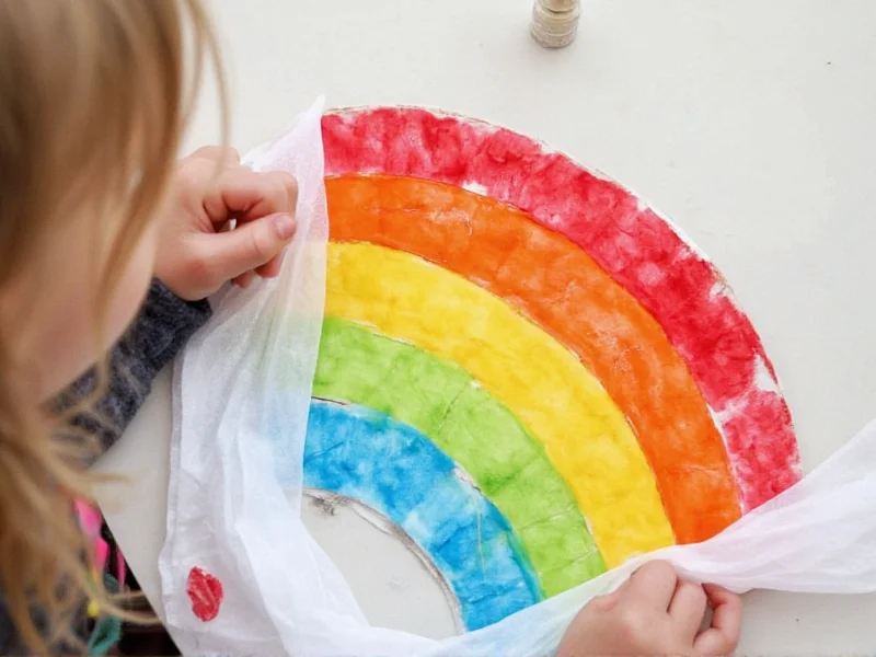 Child creating rainbow sun catcher with paper plate