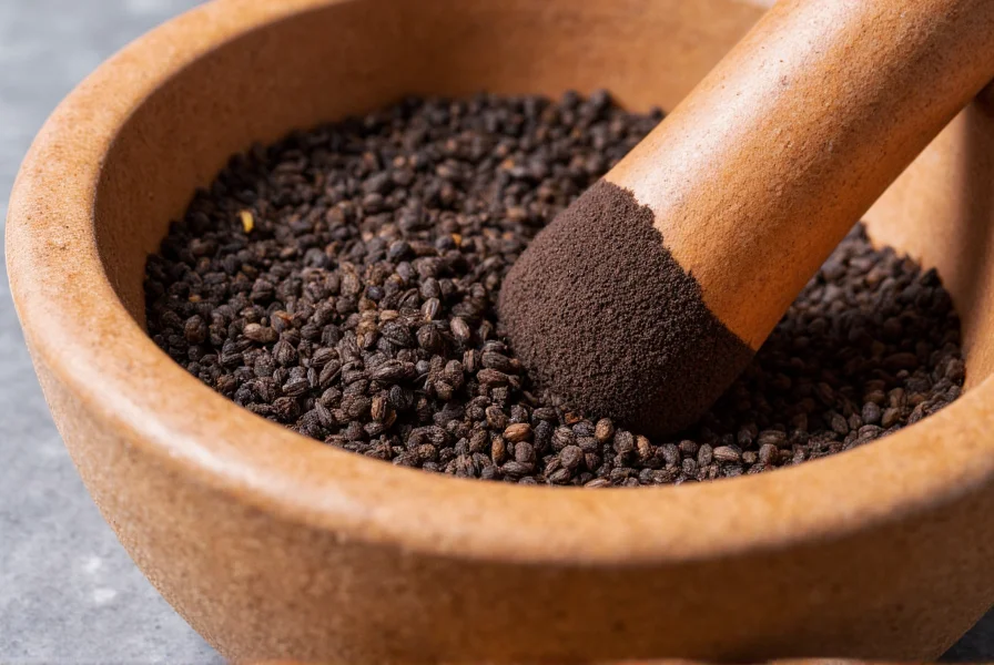 Traditional mortar and pestle with black cumin seeds being ground, showing the dark powder against the stone surface
