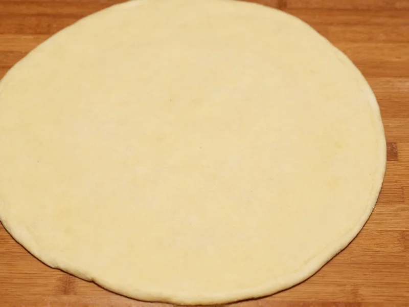 Homemade noodle dough rolled thin on wooden surface