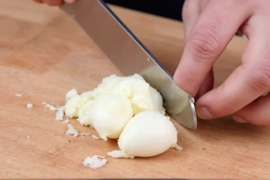 Proper technique for mincing garlic with chef's knife showing hand position and garlic texture