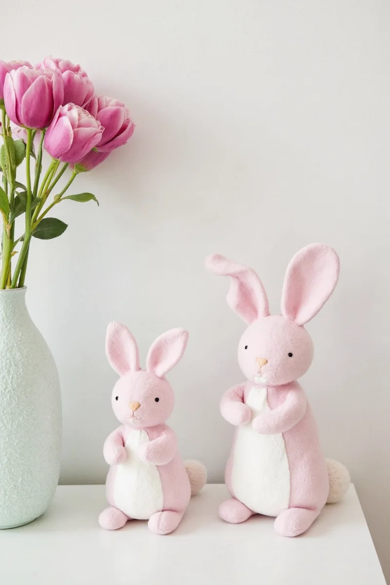 A soft pink bedroom featuring bunny-shaped nightlights, printed curtains, and a small hopping zone next to the bed.