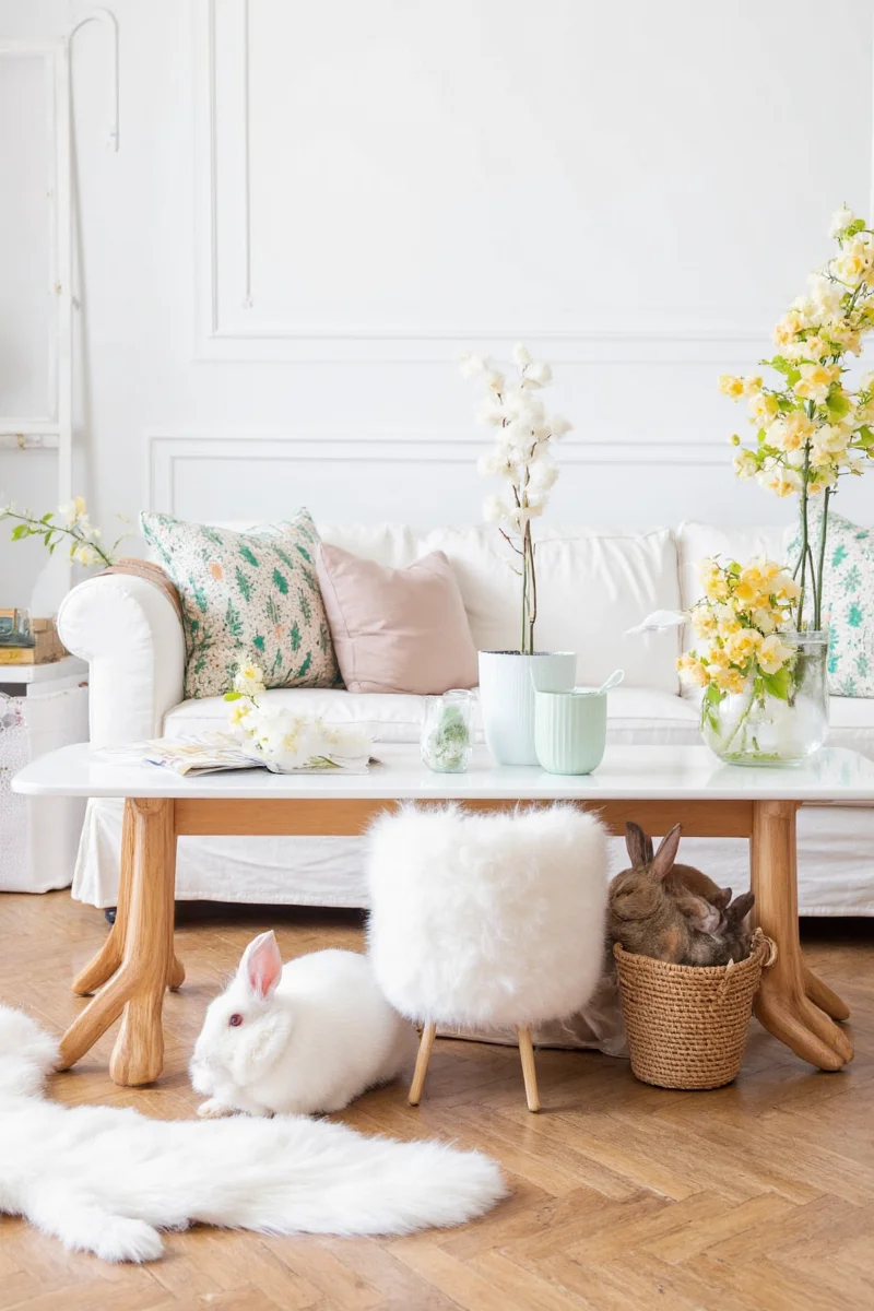 A living room decorated with rabbit-safe furniture, including a wooden coffee table and woven rug. Two bunnies are seen lounging nearby.