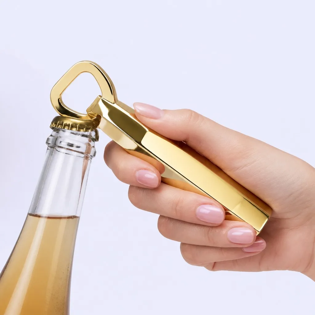 Hand using the faceted gold bottle opener to open a clear glass bottle