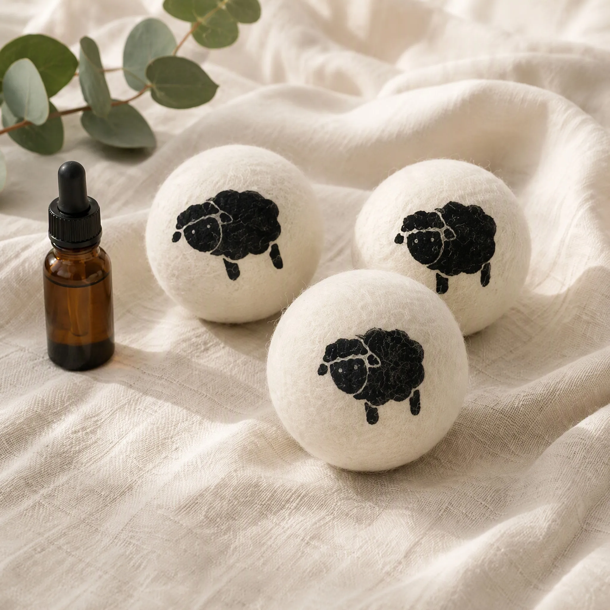 Wool dryer balls printed with a solid black sheep silhouette beside a bottle of essential oil on linen