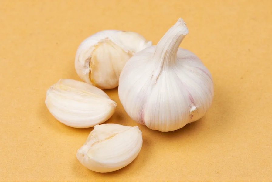 Chef's knife pressing down on garlic clove to loosen skin