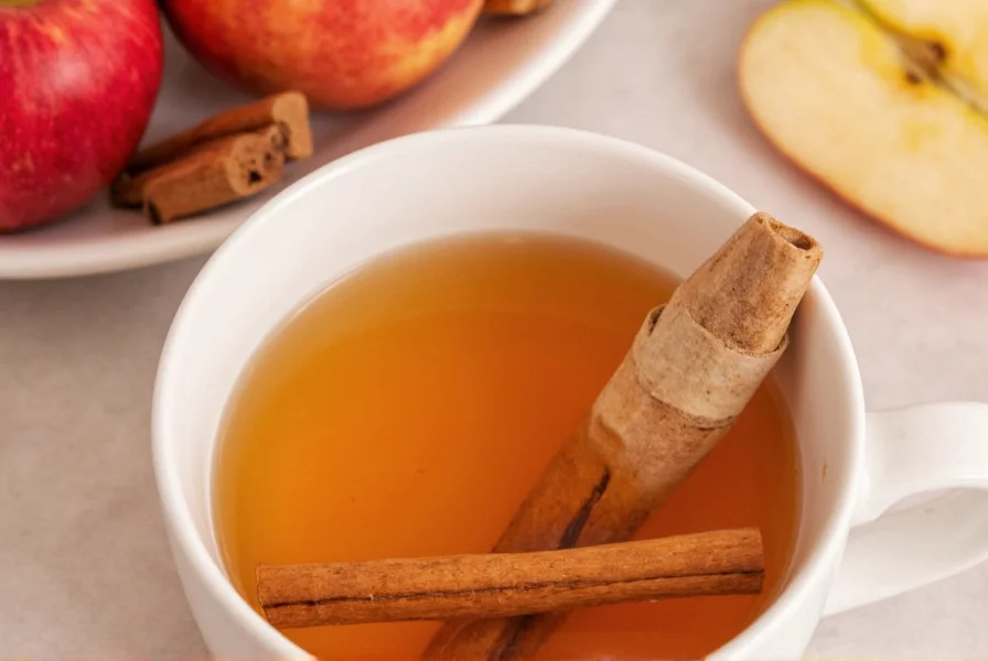 Freshly brewed apple cinnamon tea in a white ceramic mug with cinnamon sticks and apple slices garnish on wooden table