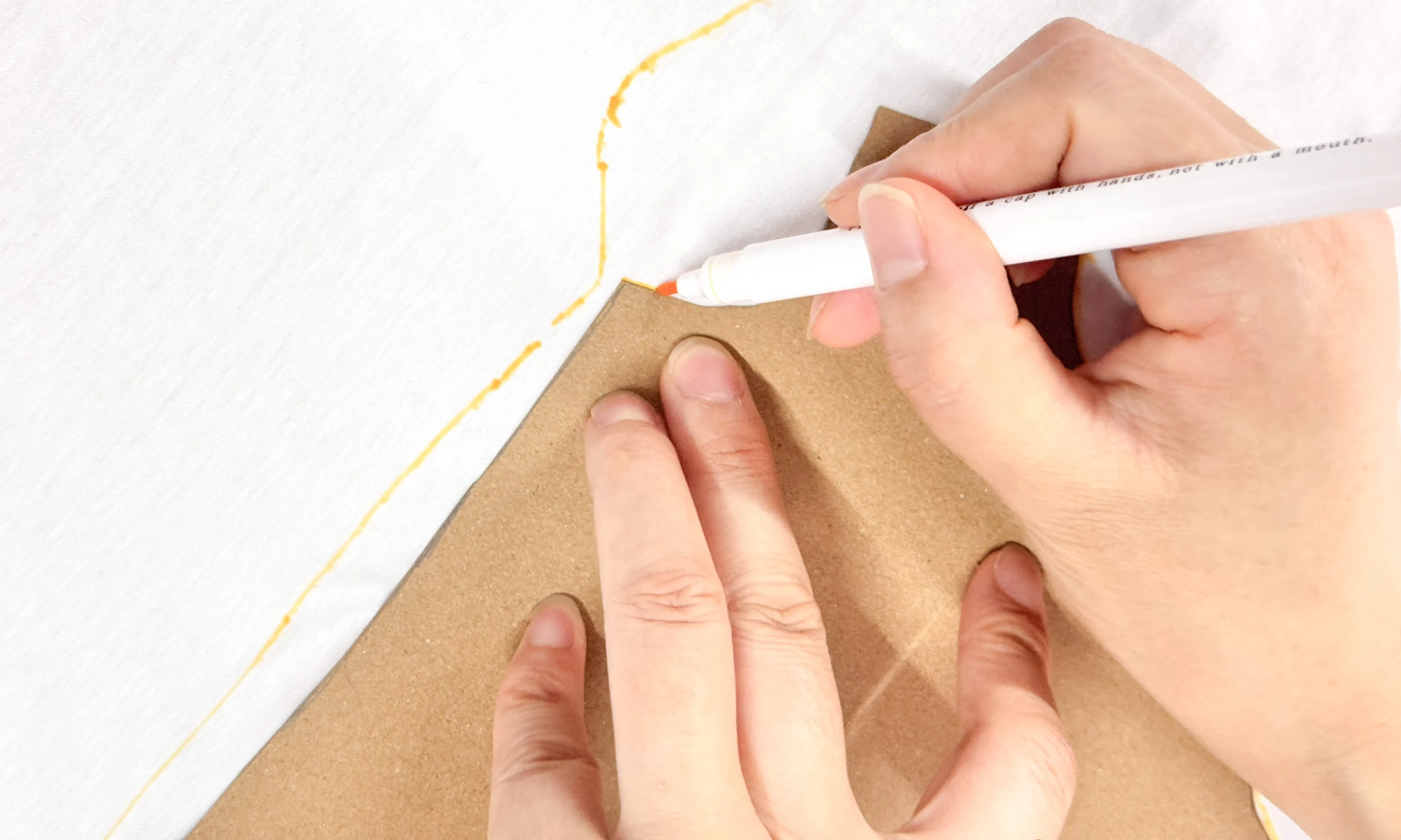 Tracing cardboard template onto white fabric with orange fabric marker