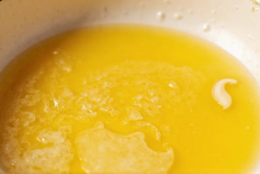 Close-up of golden brown butter bubbling in a light-colored saucepan with visible milk solids separating