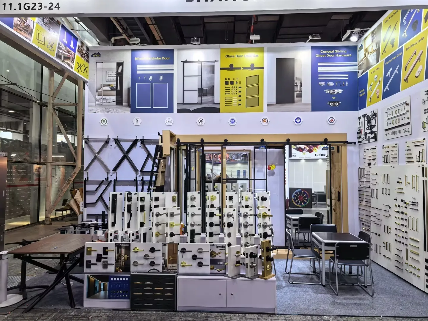 Vue d'ensemble du stand Wekis 11.1 G23-24 à la Foire de Canton, présentant l'intégralité de la gamme de quincaillerie pour portes et poignées de meubles exposée sur un mur.