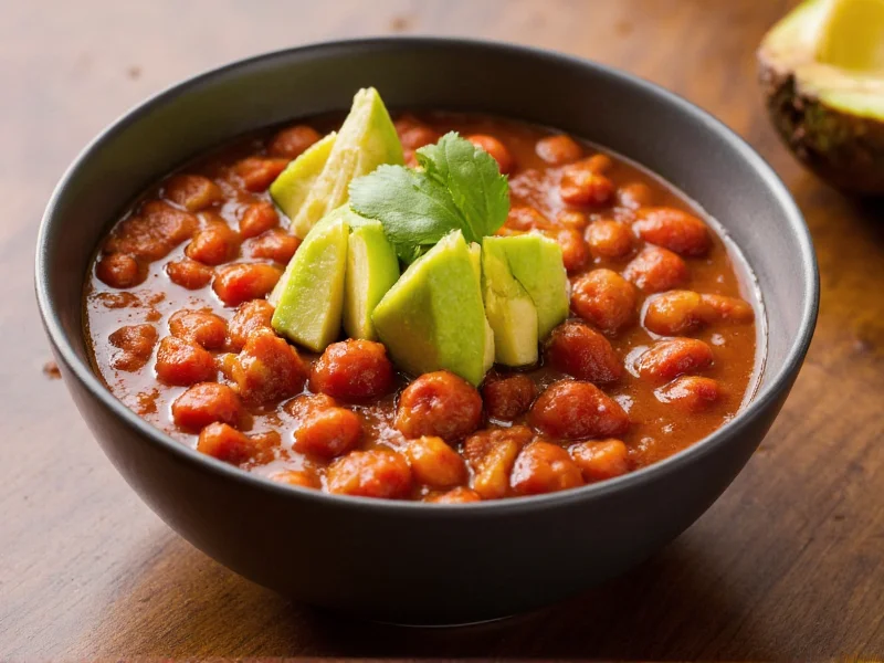 Bowl of chili with avocado and lime garnish on wooden table