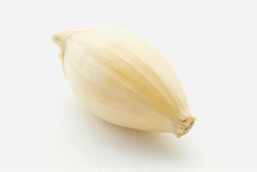 Close-up photograph of a single peeled garlic clove next to an unpeeled clove showing the papery skin