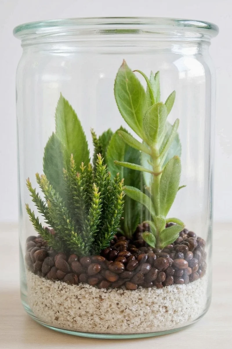 A clear cube terrarium with fake tree branches and treat pockets for birds, placed on a sturdy wooden stand.