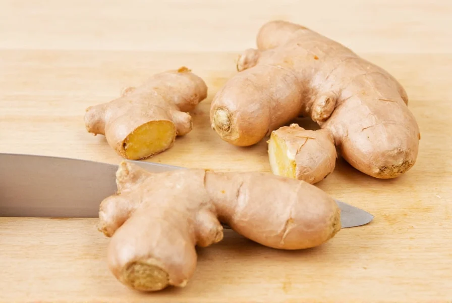 Chef's knife chopping thin ginger slices into fine mince on wooden cutting board
