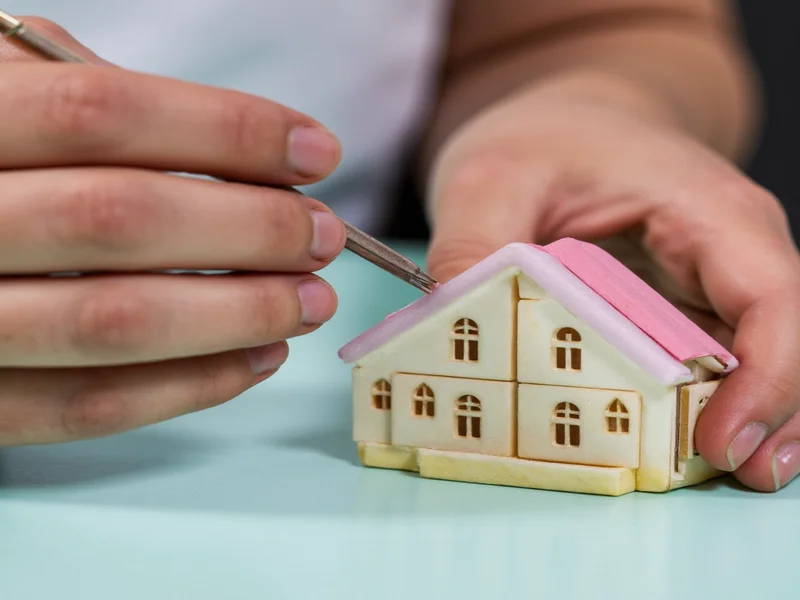 Close-up of hands assembling miniature house kit with tweezers