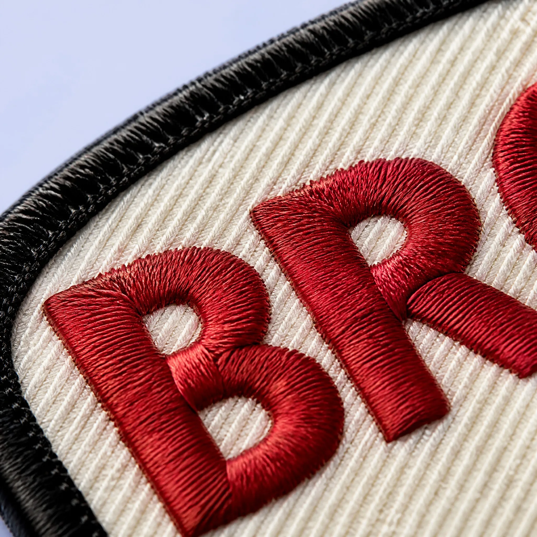 4K Macro Close-up of 3D Red Satin Stitched Lettering on Off-White Diagonal Polyester Twill Background with Black Merrowed Rim