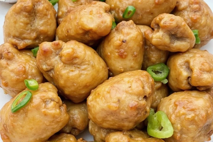 Finished ginger chicken dish with glossy sauce coating chicken pieces and fresh scallions on white plate