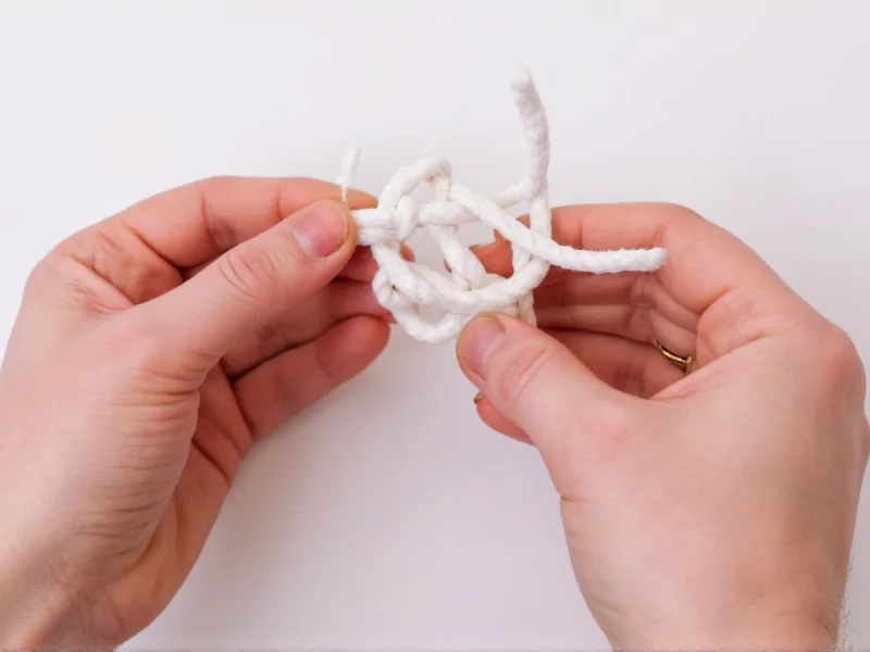 Hands demonstrating square knot technique with cotton rope
