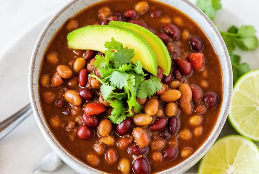 Three bean chili served in bowl with toppings including avocado, cilantro, and lime wedges